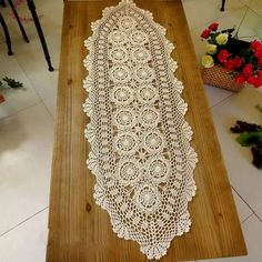 a table runner with white crocheted doily on it and flowers in the background