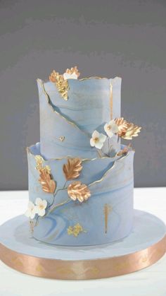 a three tiered blue cake with gold leaves and flowers