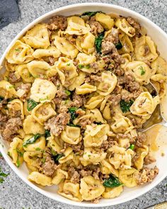 a white bowl filled with pasta and meat on top of a gray table next to silverware