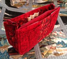 a red purse sitting on top of a quilted tablecloth covered bed with two candles in it