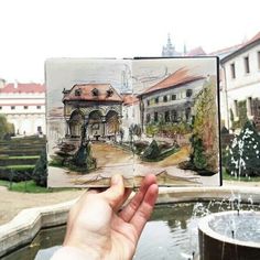 a hand holding up an open book in front of a fountain