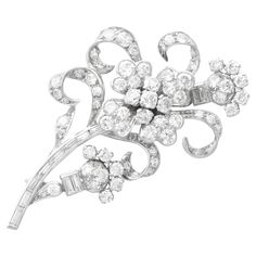 A stunning, fine and impressive antique 1920s 5.85 carat diamond and 15 karat white gold floral brooch; part of our diverse diamond flower brooches and jewellery collections. This fine and impressive antique diamond brooch has been crafted in 15k white gold. The diamond spray brooch is embellished with a central quatrefoil shaped design incorporating five individually claw set Old European cut diamonds in relief to four lobed petal designs, each embellished with four further pavé set diamonds. The elongated stem is comprised of nine channel set baguette cut diamonds, accented with scrolling leaf designs incorporating thirty-four pavé set Old European cut diamonds. This stunning brooch is further ornamented with two bud designs, each bearing a combination of Old European and baguette cut di Diamond Flower Brooch, Plant Jewelry, Floral Brooch, Brooch Bouquets, Diamond Brooch, Baguette Cut Diamond, Gold Brooches, European Cut Diamonds, Diamond Flower