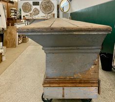 an old gray stone pedestal in the middle of a store floor with other items on display behind it