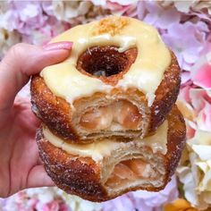 a person holding two doughnuts with icing and nuts on them in front of flowers