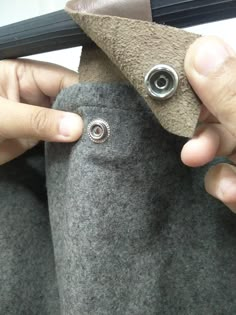 two hands are working on a piece of fabric with metal pins in the bottom corner