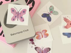 some cards with butterflies on them are laying next to a box that says saturnpop club