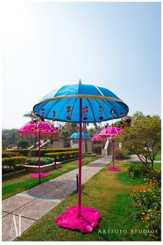 a blue umbrella sitting on top of a lush green park covered in pink flowers and grass