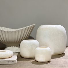 three white vases sitting on top of a table next to a bowl and book