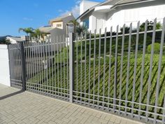 an iron fence is in front of a white house with green bushes on the side