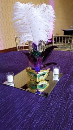 a table topped with a purple cloth covered tablecloth and a vase filled with feathers