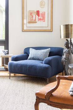 a blue chair sitting in front of a window next to a table with a lamp on it