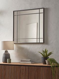 a mirror is hanging on the wall above a dresser with books and plants in it