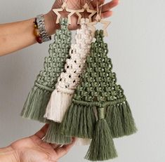 two hands holding small green and white tasseled ornaments with stars on them, one in the shape of a christmas tree