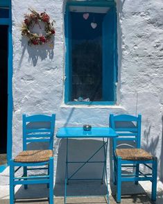 two blue chairs and a table in front of a white building with a blue window