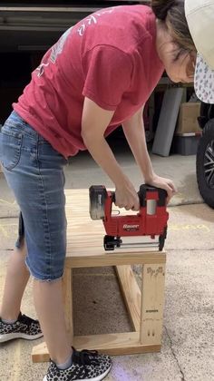 a woman using a driller on a table with a bench made out of pallets