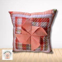 an orange and white plaid pillow with a flower on the front, sitting on a wooden floor