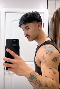 a man taking a selfie with his cell phone in the mirror while wearing a black tank top