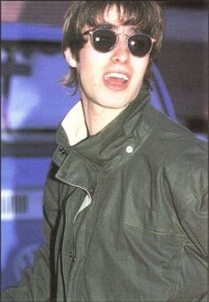 a young man wearing sunglasses and a green jacket is making a face with his mouth open