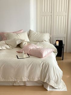 a bed with white sheets and pink pillows