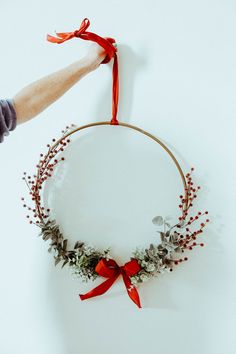 someone is holding a wreath with red ribbon and berries on the front, while another hand holds