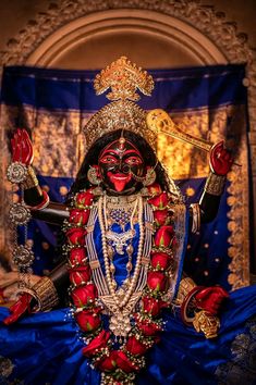 an idol is displayed in front of a blue curtain with gold trimmings and red roses