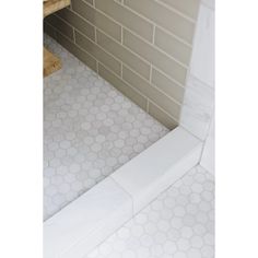 a white tiled bathroom with hexagonal tiles on the walls and floor, along with a bench