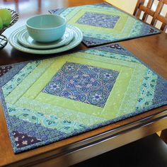 a wooden table topped with two place mats covered in blue and green quilted squares