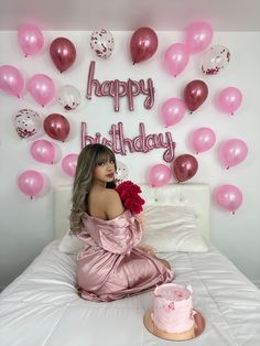 a woman sitting on top of a bed next to a pink cake and balloon wall