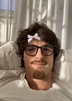 a man with glasses and a bow in his hair is laying down on a bed