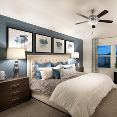 a bedroom with blue walls and pictures on the wall above the bed, along with a ceiling fan