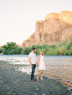 a man and woman standing next to each other on the shore of a body of water