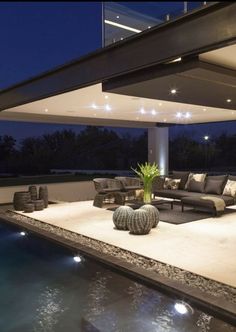 an outdoor living area with couches and tables next to a swimming pool at night