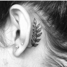 a black and white photo of a woman's ear with a small leaf tattoo on it