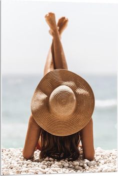 a woman laying on the beach with her arms behind her head wearing a straw hat