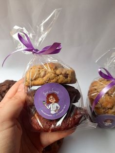 a person holding some cookies and chocolate chip cookies in plastic bags with purple ribbon around them