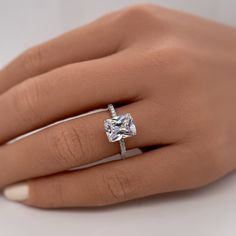 a woman's hand with a white diamond ring on her left hand and the other hand holding an engagement ring