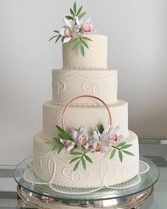 a three tiered cake with flowers on the side and a ring at the top