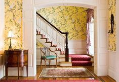 an entry way with floral wallpaper and rugs on the hardwood floor, along with a stair case