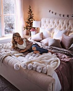 a woman laying on top of a bed next to a christmas tree in a bedroom