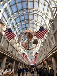 people are walking through an airport with american flags hanging from the ceiling and glass windows