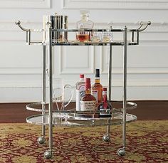 a bar cart with liquor bottles and glasses on the bottom shelf in front of a rug