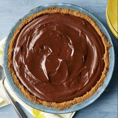 a pie with chocolate frosting in a blue dish on a table next to two yellow plates