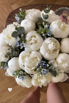 a bridal bouquet with white flowers and greenery in someone's hand on a wooden floor