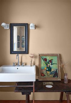 a bathroom with a sink, mirror and painting on the wall in front of it