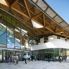 people are walking around in front of a building with glass walls and wooden roofing