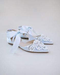 a pair of white shoes with bows and pearls on the toes are shown in front of a plain background