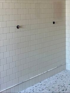 an empty bathroom with white tiles and black handles on the wall, in front of a tiled shower stall