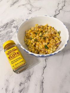 a white bowl filled with food next to a jar of seasoning on top of a marble counter