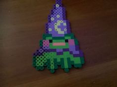 a purple and green piece of art made out of perler beads on a wooden table