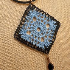 a blue and black crochet square on a leather cord with a tassel hanging from it